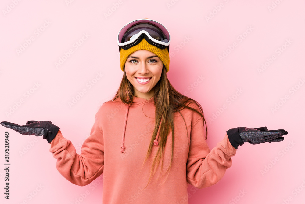Young caucasian woman wearing a ski clothes isolated makes scale with arms, feels happy and confident. Young caucasian woman wearing a ski clothes isolated makes scale with arms, feels happy and confident.