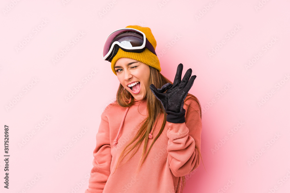 Young caucasian woman wearing a ski clothes isolated winks an eye and holds an okay gesture with hand. Young caucasian woman wearing a ski clothes isolated winks an eye and holds an okay gesture with hand.