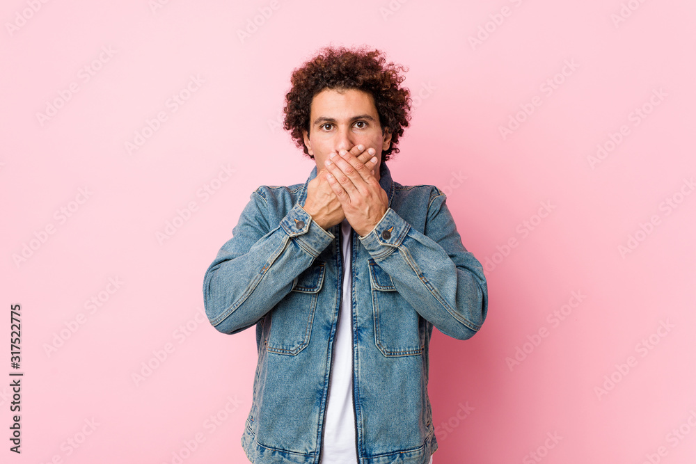 Curly mature man wearing a denim jacket against pink background shocked covering mouth with hands. Curly mature man wearing a denim jacket against pink background shocked covering mouth with hands.