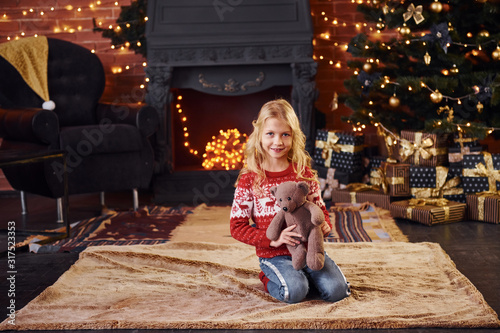 Cute little girl in red festive sweater with teddy bear indoors celebrating new year and christmas holidays