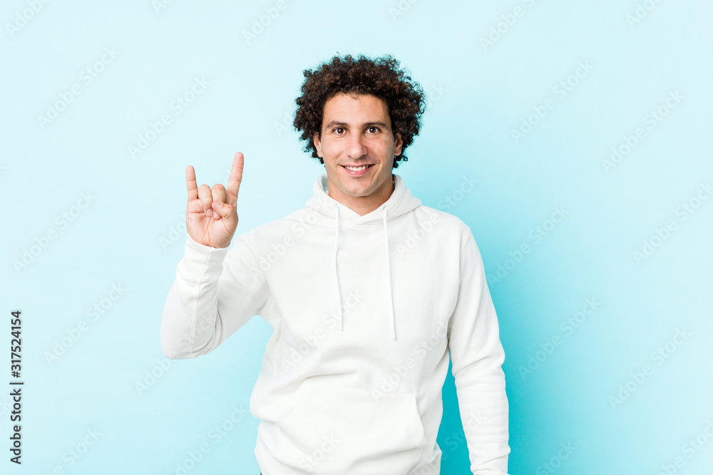 Young sporty man against a blue background showing a horns gesture as a revolution concept. Young sporty man against a blue background showing a horns gesture as a revolution concept.