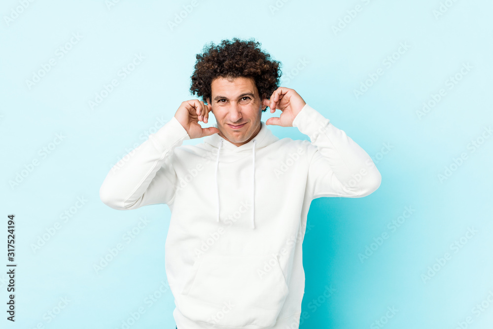 Young sporty man against a blue background covering ears with hands. Young sporty man against a blue background covering ears with hands.