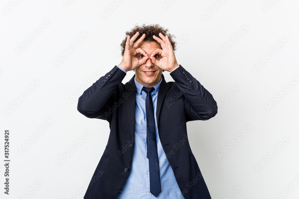 Young business curly man against white background showing okay sign over eyes Young business curly man against white background showing okay sign over eyes