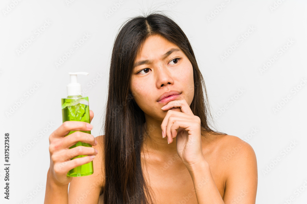 Young chinese woman holding a moisturizer with aloe vera isolated looking sideways with doubtful and skeptical expression. Young chinese woman holding a moisturizer with aloe vera isolated looking sideways with doubtful and skeptical expression.