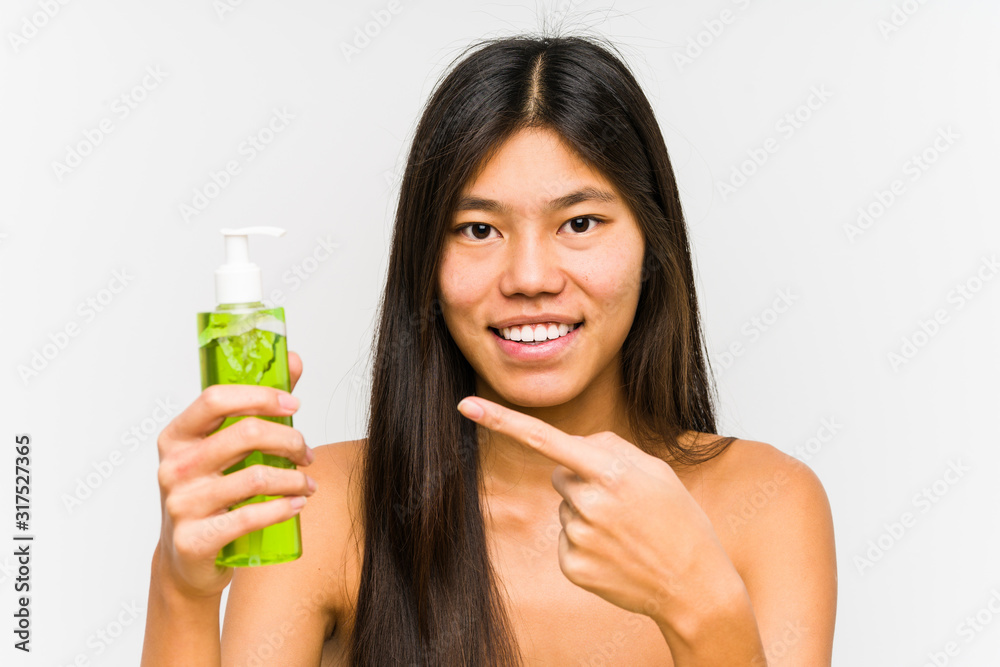 Young chinese woman holding a moisturizer with aloe vera isolated smiling cheerfully pointing with forefinger away. Young chinese woman holding a moisturizer with aloe vera isolated smiling cheerfully pointing with forefinger away.
