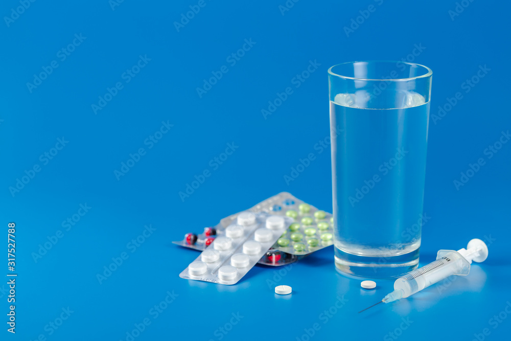 Glass with water, pills, syringe on blue background with copy space Glass with water, pills, syringe on blue background with copy space
