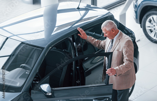 Aged man in formal wear walking in the automobile salon and looking for the car © standret