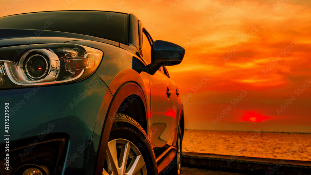 Blue compact SUV car with sport and modern design parked on concrete road by the sea beach at sunset. Front view of luxury car. New SUV car with beautiful red sunset sky and clouds at the beach.