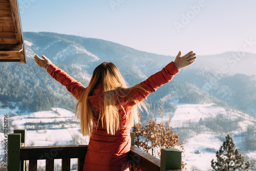 Woman standing with her hands raised facing the mountains in winter time #317528716