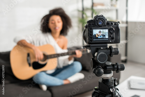 selective focus of digital camera with young african american girl in braces playing acoustic guitar and singing on display