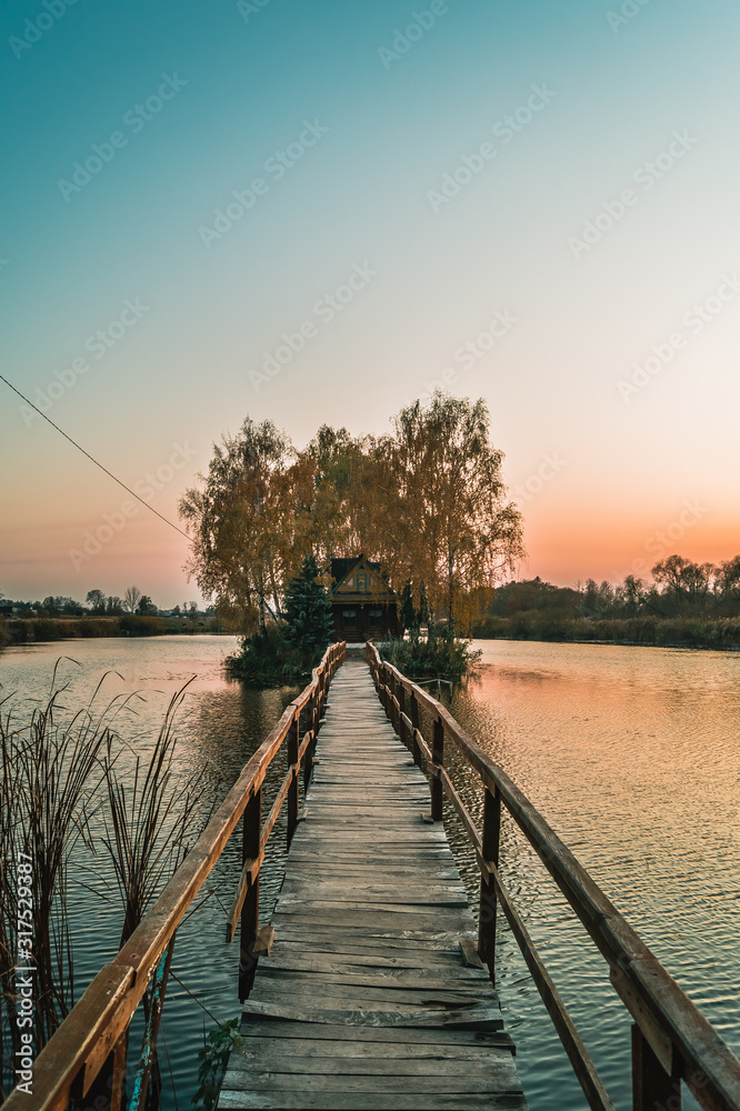 Fototapeta premium Wooden bridge to the fisherman's house on the river island at sunset