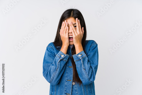 Young asian woman blink through fingers frightened and nervous.