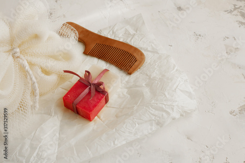 Beautifully packaged natural pink and white soap in colored ribbon, natural loofah and wooden hair comb with cloves on a light decorative background. Natural self care concept. Selective focus