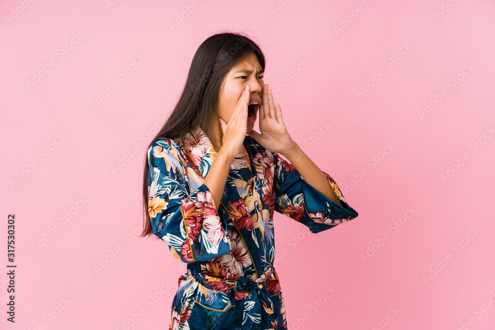 Young asian woman wearing a kimono pajamas shouts loud, keeps eyes opened and hands tense. Young asian woman wearing a kimono pajamas shouts loud, keeps eyes opened and hands tense.