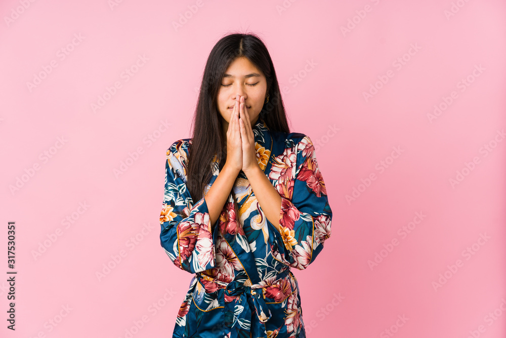 Young asian woman wearing a kimono pajamas holding hands in pray near mouth, feels confident. Young asian woman wearing a kimono pajamas holding hands in pray near mouth, feels confident.