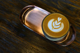 A cup of latte art coffee in brass plate on wooden table