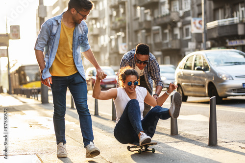 Group of friends hangout at the city street.Female sitting on skate board while friends pushing her from behind. 