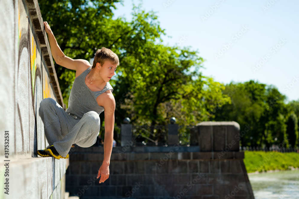 Obraz premium Young man in sportswear practicing parkour outside on stone wall on clear summer day
