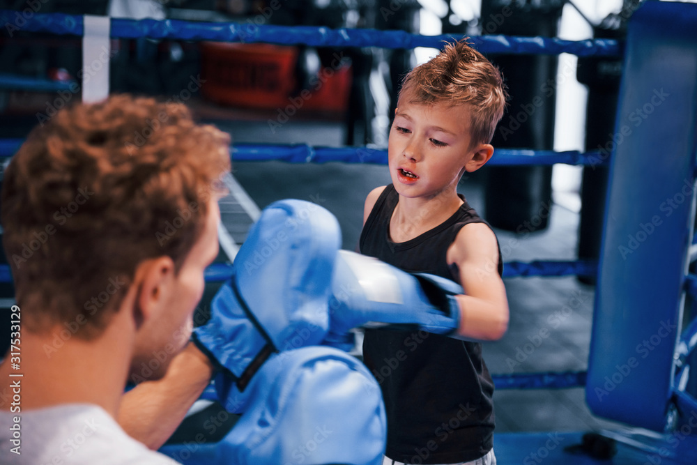 Fototapeta premium Young boxing coach is helping little boy in protective wear on the ring between the rounds