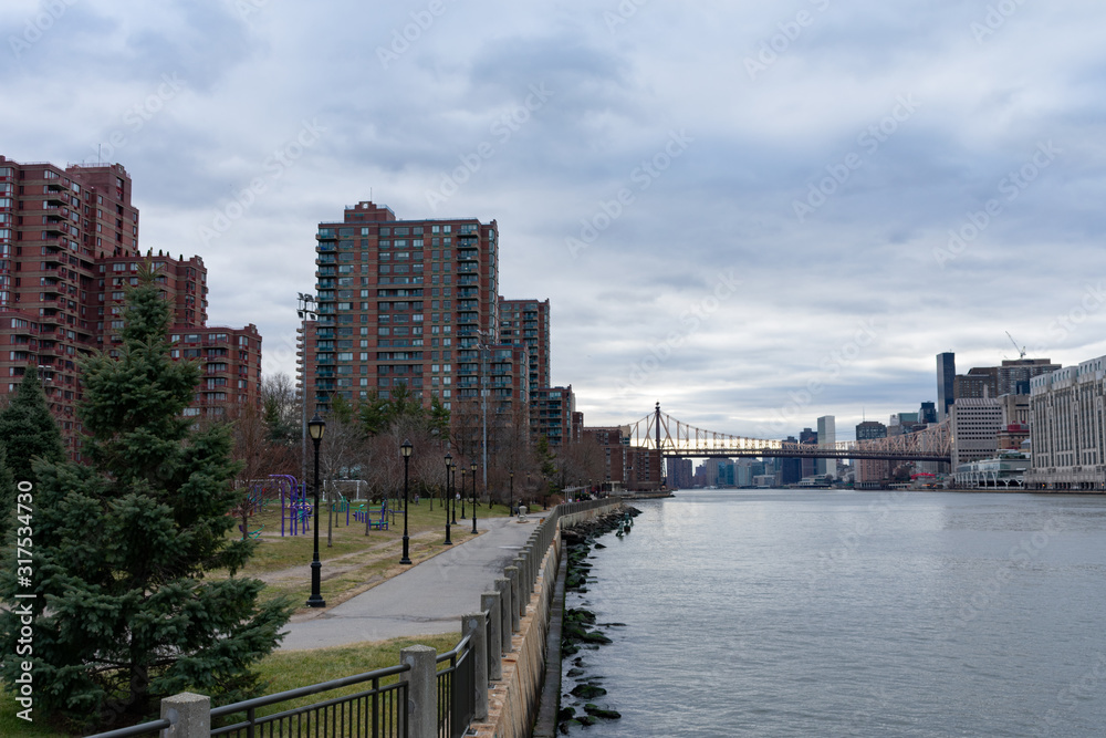 Waterfront at Roosevelt Island along the East River with the Queensboro Bridge connecting to Manhattan in New York City Waterfront at Roosevelt Island along the East River with the Queensboro Bridge connecting to Manhattan in New York City
