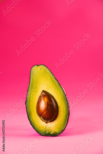 Tropical summer background. Green avocado on a pink background. Food concept. Minimal.