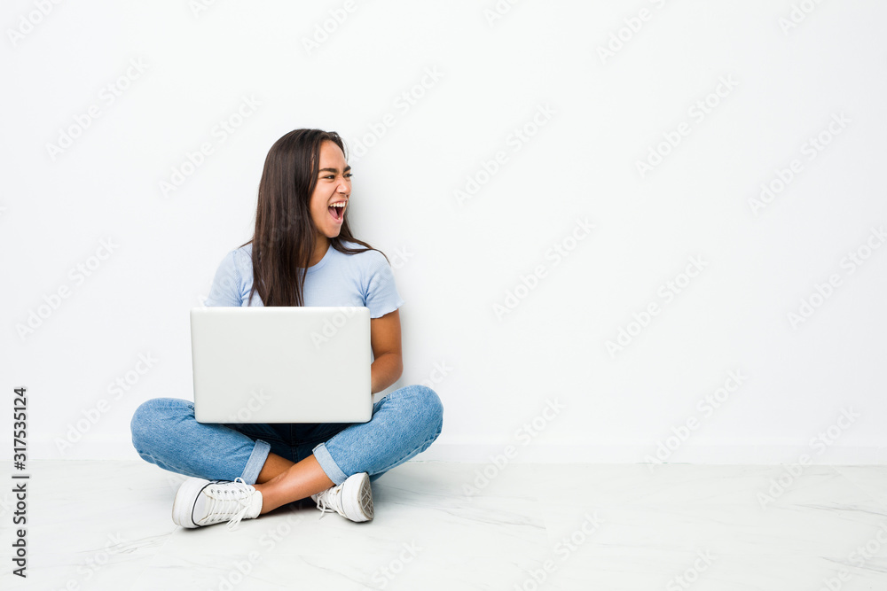 Young mixed race indian woman sitting working on laptop shouting towards a copy space