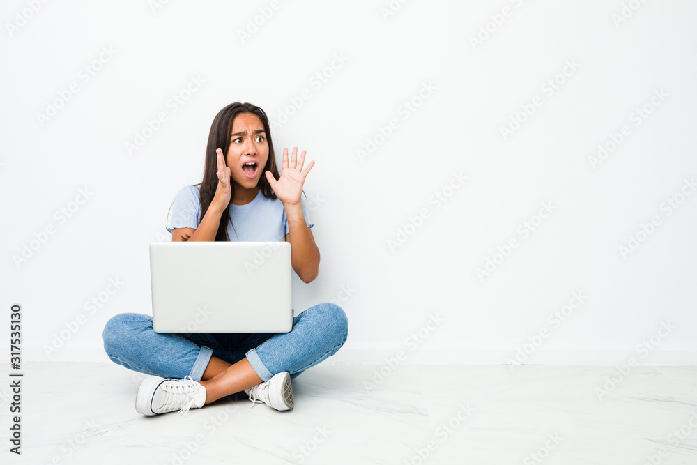 Young mixed race indian woman sitting working on laptop shouts loud, keeps eyes opened and hands tense. Young mixed race indian woman sitting working on laptop shouts loud, keeps eyes opened and hands tense.