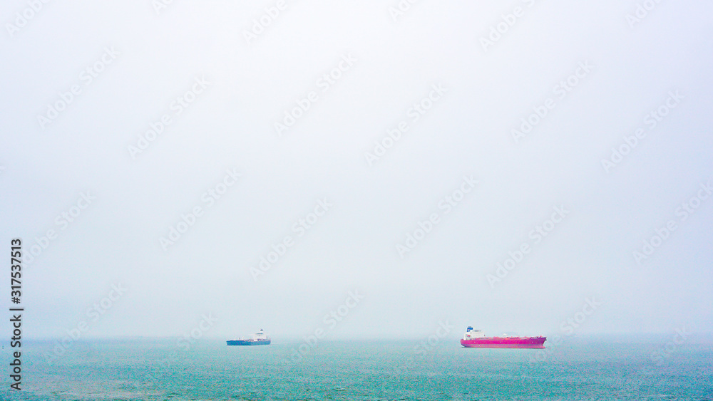 Two cargo ships at sea on a foggy afternoon.