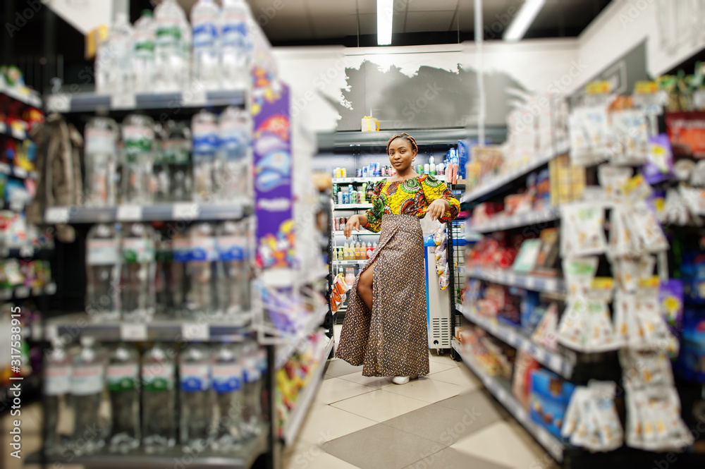 Happy african woman in traditional clothes and veil looking product at grocery store, shopping in supermarket.  Afro black  women costumer buying food at the market.