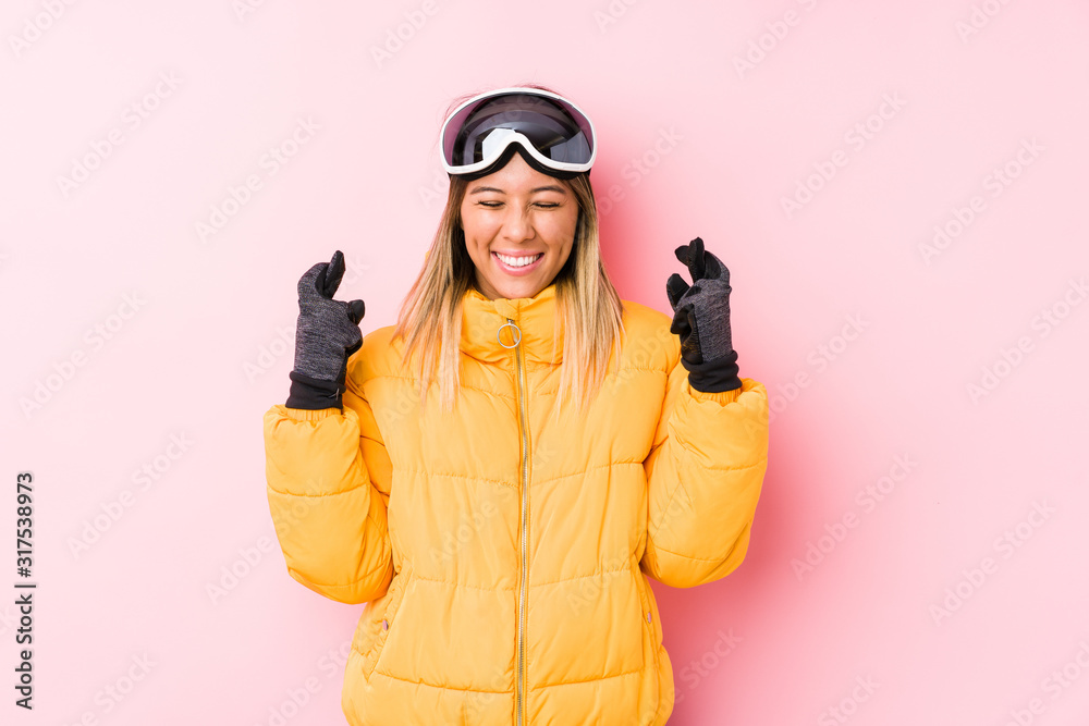 Young caucasian woman wearing a ski clothes in a pink background crossing fingers for having luck
