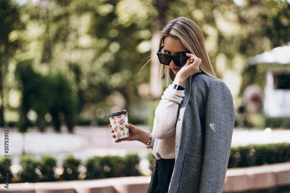 Beautiful blonde woman walking on street.Stylish smiling business woman with coffee in Dark casual trousers, creamy sweater and sunglasses.Female business style.High Resolution.