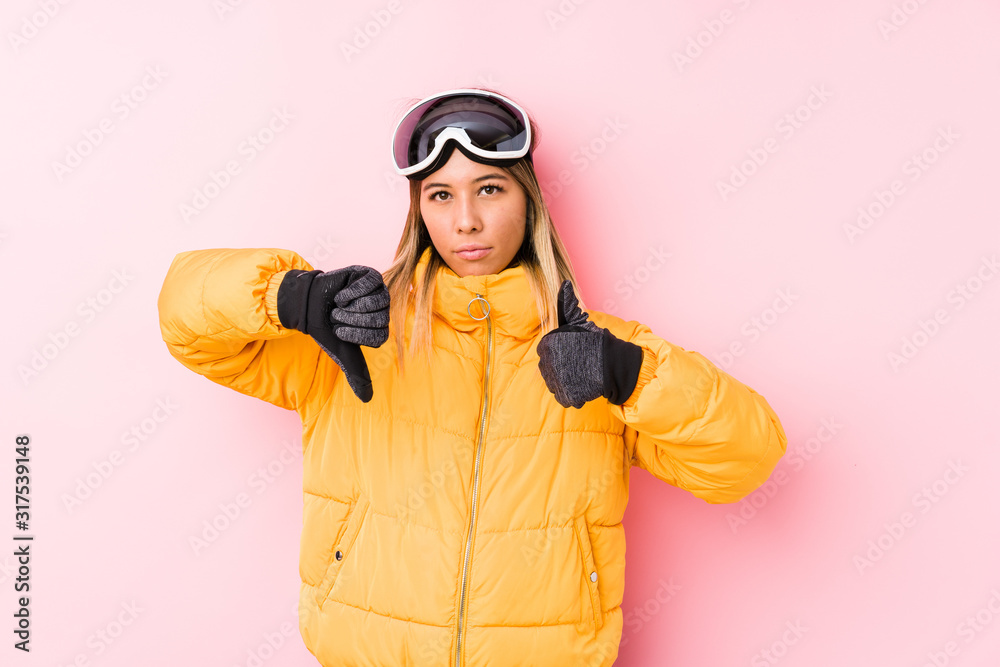 Young caucasian woman wearing a ski clothes in a pink background showing thumbs up and thumbs down, difficult choose concept
