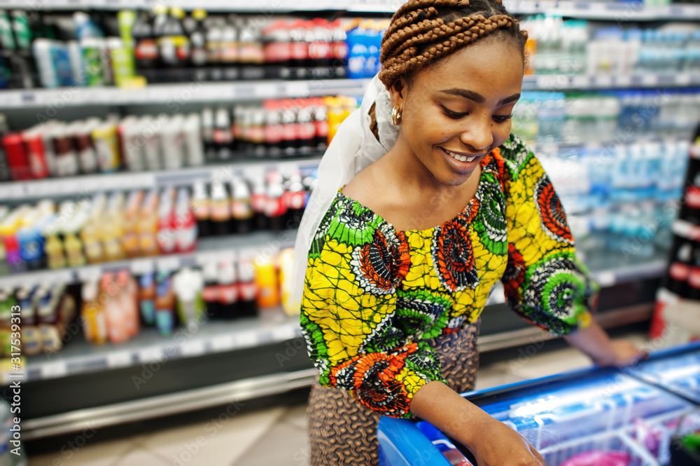 Happy african woman in traditional clothes and veil looking product at grocery store, shopping in supermarket.  Afro black  women costumer buying food at the market.