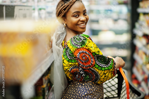 Canvas Print Happy african woman in traditional clothes and veil looking product at grocery store, shopping in supermarket