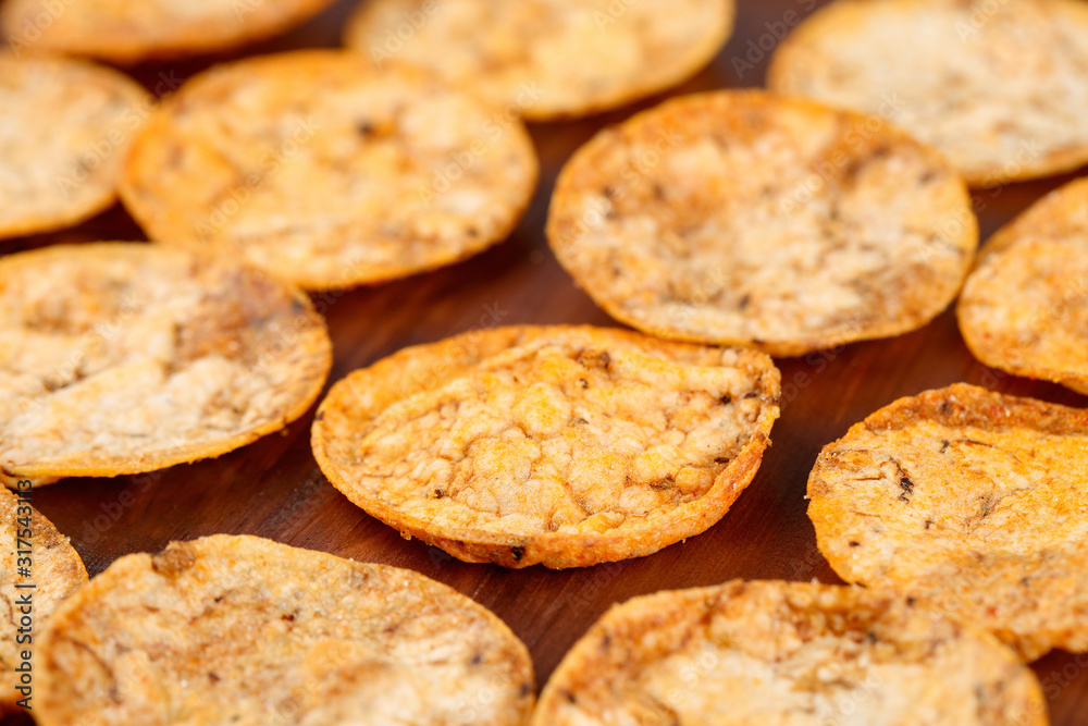 Close up of organic, crispy, baked, whole grain rice chips with tomato and paprika spices. Gluten free healthy snack on a wooden background. Selective focus and very shallow depth of field