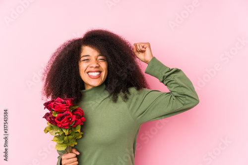 Young afro woman holding a roses isolated Young afro woman holding a rosesraising fist after a victory, winner concept.