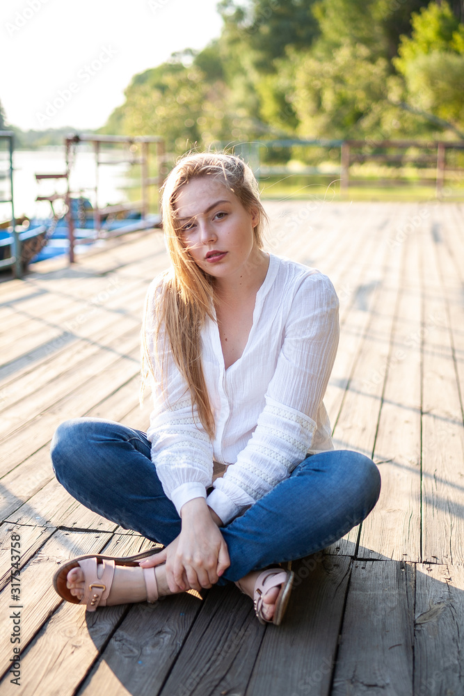 Beautiful girl sitting on wooden floor at sunset