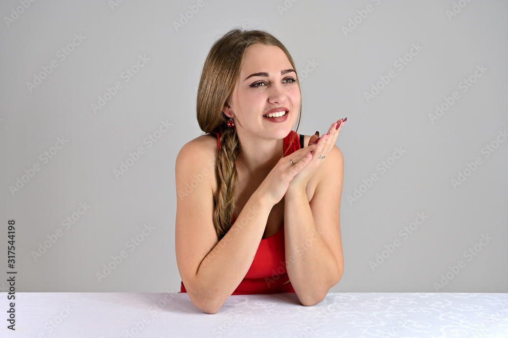 Horizontal photo of a pretty smiling girl with long hair and great makeup sitting at a white table in the studio. Universal concept female portrait on a white background. Horizontal photo of a pretty smiling girl with long hair and great makeup sitting at a white table in the studio. Universal concept female portrait on a white background.