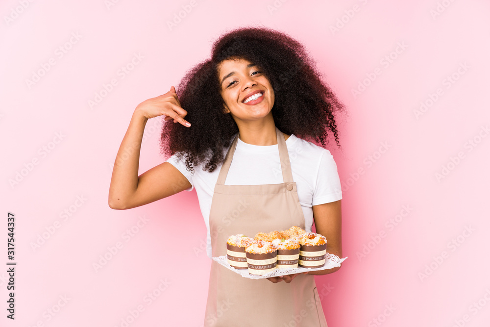 Young afro pastry maker woman holding a cupcakes isolatedYoung afro baker woman showing a mobile phone call gesture with fingers. Young afro pastry maker woman holding a cupcakes isolatedYoung afro baker woman showing a mobile phone call gesture with fingers.