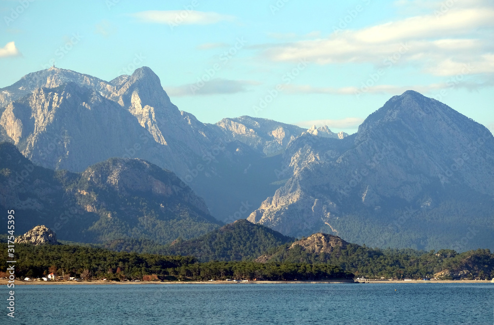 Beautiful landscape with calm sea, coastline, and high mountains covered with green forests