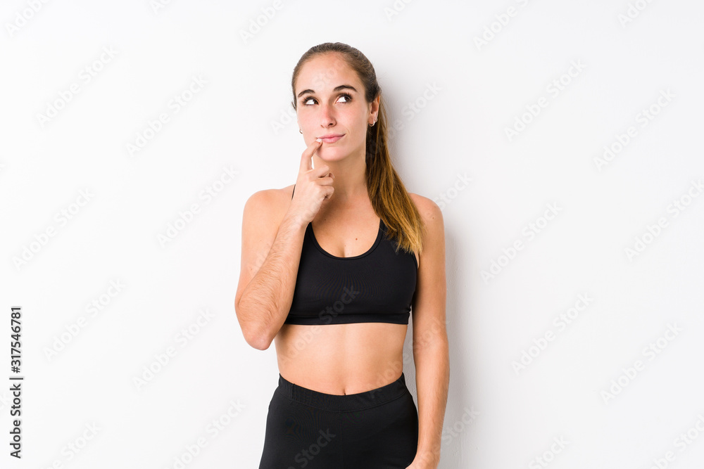 Young caucasian fitness woman posing in a white background looking sideways with doubtful and skeptical expression. Young caucasian fitness woman posing in a white background looking sideways with doubtful and skeptical expression.