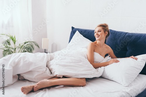 beautiful smiling woman lying in sheets on bed in morning