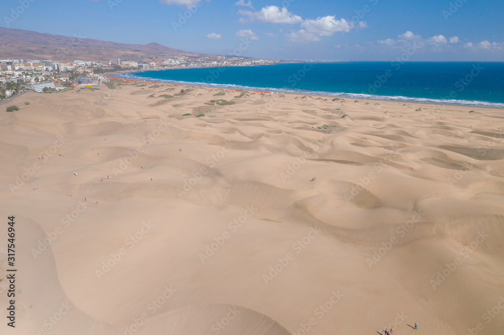 Scenic cinematic aerial view of Maspalomas sand dunes on seacoast on Gran Canaria island in Spain. Beautiful summer sunny look of white sand and sea of one of Canary islands.