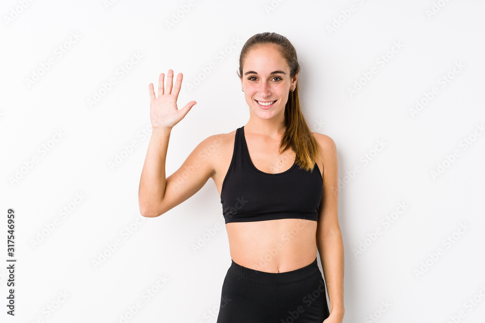 Young caucasian fitness woman posing in a white background smiling cheerful showing number five with fingers. Young caucasian fitness woman posing in a white background smiling cheerful showing number five with fingers.