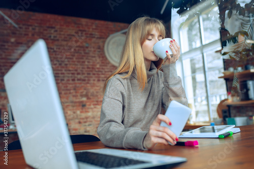Beautiful caucasian business lady working in office with laptop. Young female model in co-working place makes notes, drinks coffee, performes tasks. Concept of business, finance, freelance, open space
