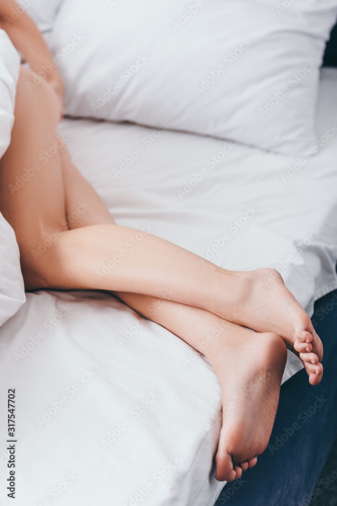 cropped view of woman lying on bed with white sheets cropped view of woman lying on bed with white sheets