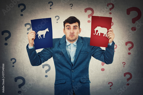 Canvas Print Undecided young man holding two brochures has to choose between donkeys and elephants