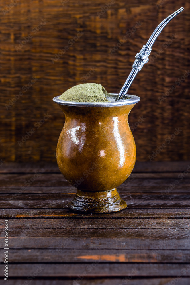 Chimarrão, or mate herb, is a South American drink left by indigenous cultures. It consists of a gourd, a pump, ground yerba mate and boiling water. Chimarrão isolated on wooden background. Copy space Chimarrão, or mate herb, is a South American drink left by indigenous cultures. It consists of a gourd, a pump, ground yerba mate and boiling water. Chimarrão isolated on wooden background. Copy space