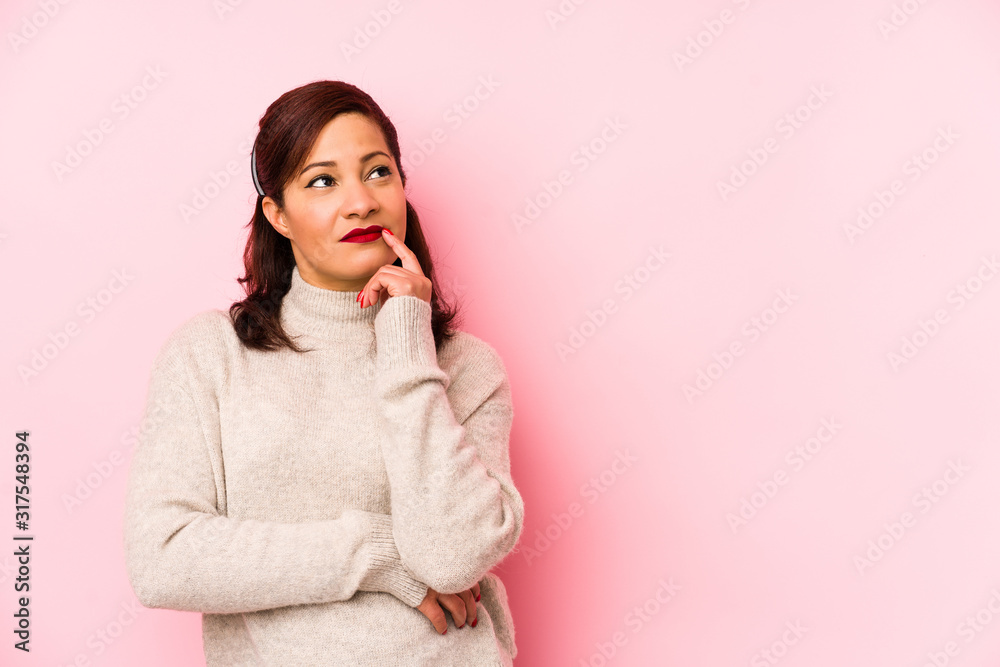 Fototapeta premium Middle age latin woman isolated on a pink background looking sideways with doubtful and skeptical expression.