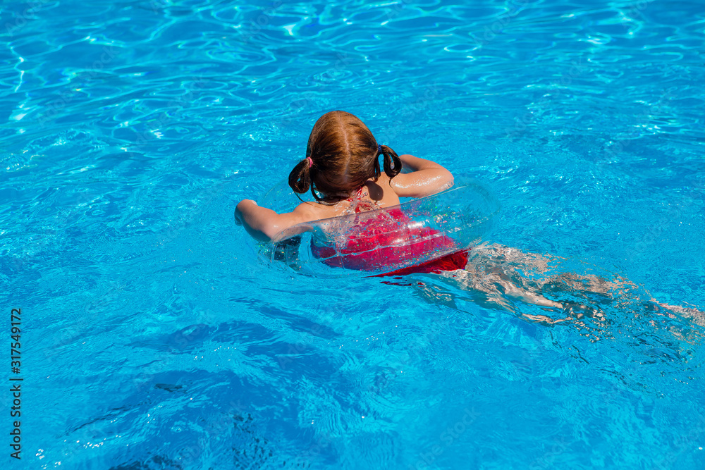 little redhead girl swims on a transparent swimming circle